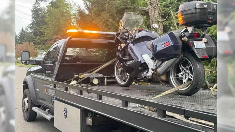 A dark blue touring motorcycle secured on the flatbed of a Century tow truck on a residential street.