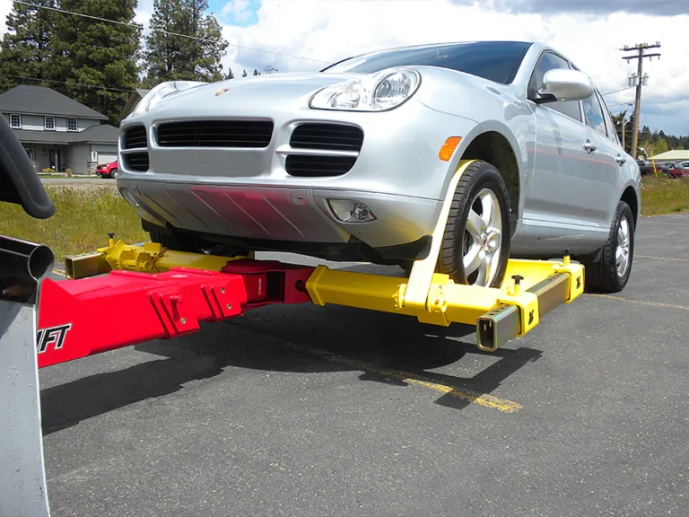 A silver SUV being towed by a yellow and red wheel-lift towing apparatus on an asphalt road.